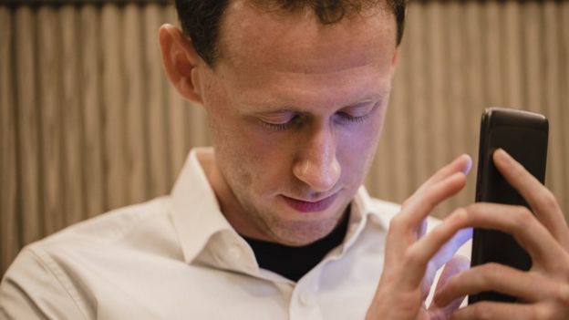 A close-up of a man wearing casual clothing, he has his smartphone in his hand and he is using a visually impaired mobile app to help assist him